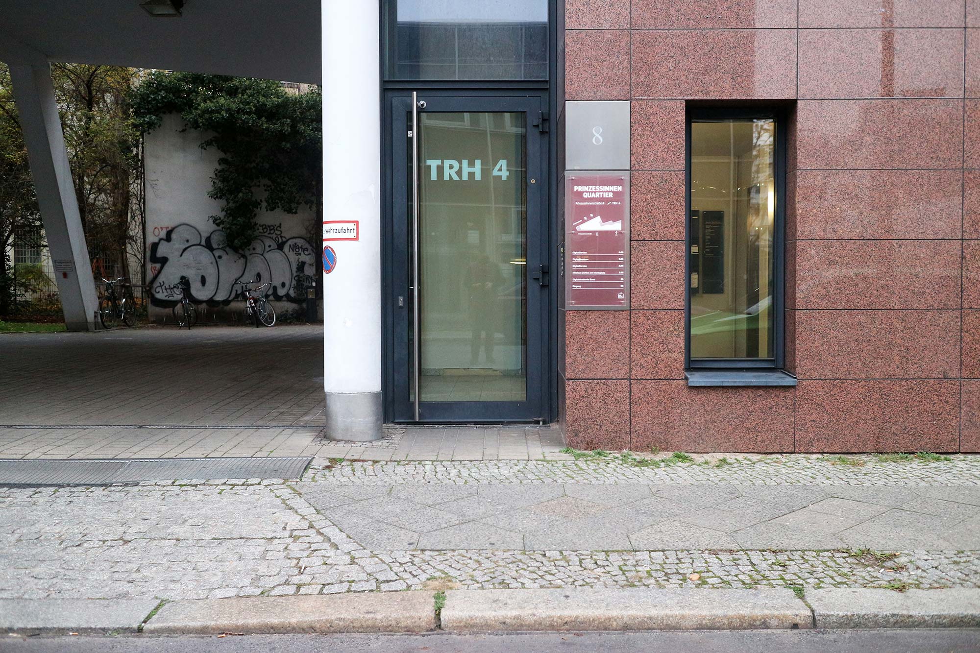 Frontal view of the office building’s main entrance; in the center there is a glass door with the inscription 