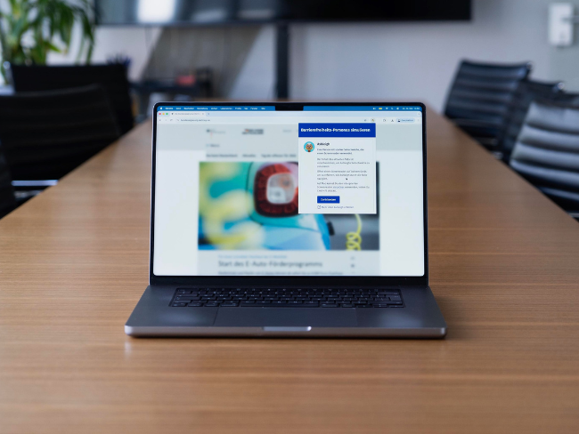 A laptop on a table displaying a severely blurred webpage in a web browser, with a window overlaid on top – featuring a visually impaired accessibility persona named Ashleigh