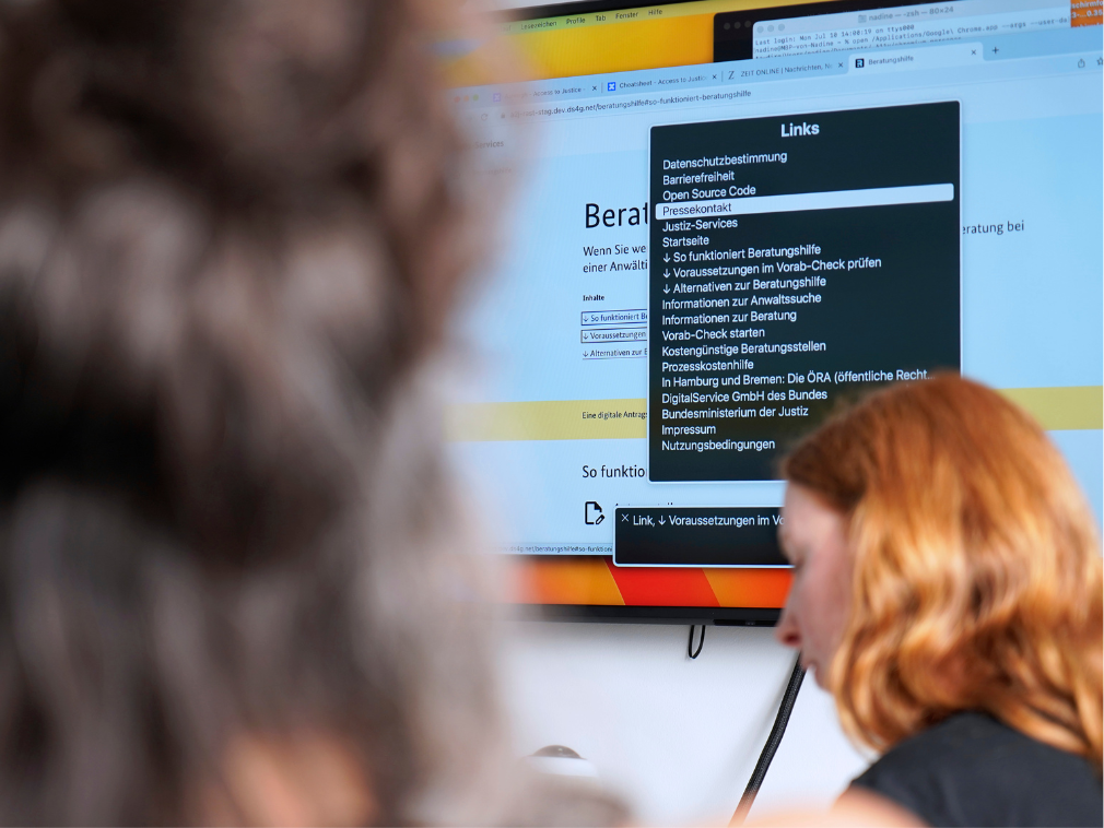 A person is sitting in front of a large screen on which an accessibility test is being carried out; another person can be seen blurred in the foreground