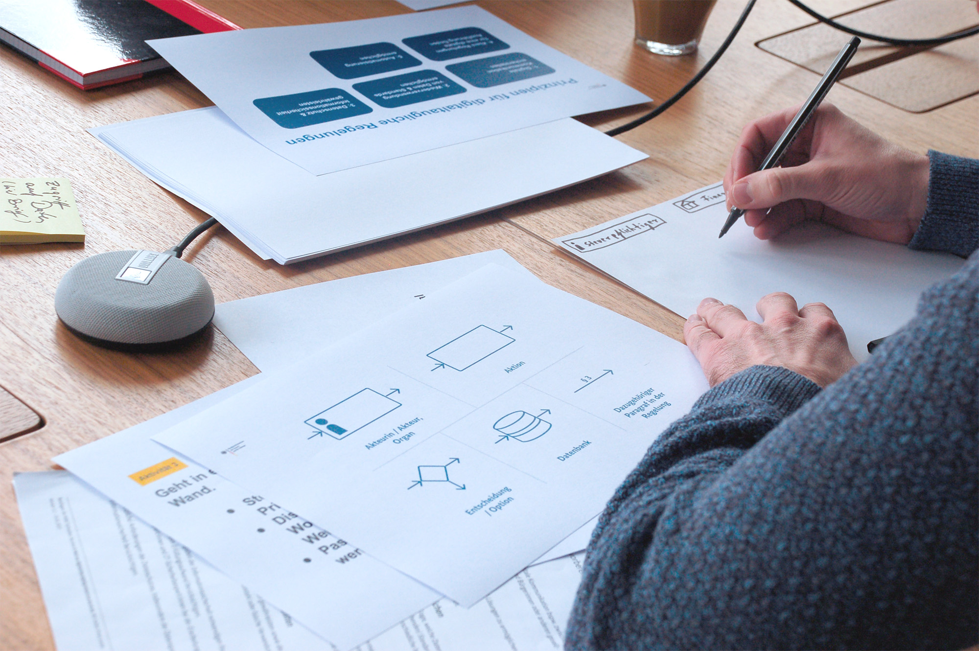 A person sits at a table and writes on a piece of paper. In front of them is a sheet showing different symbols.