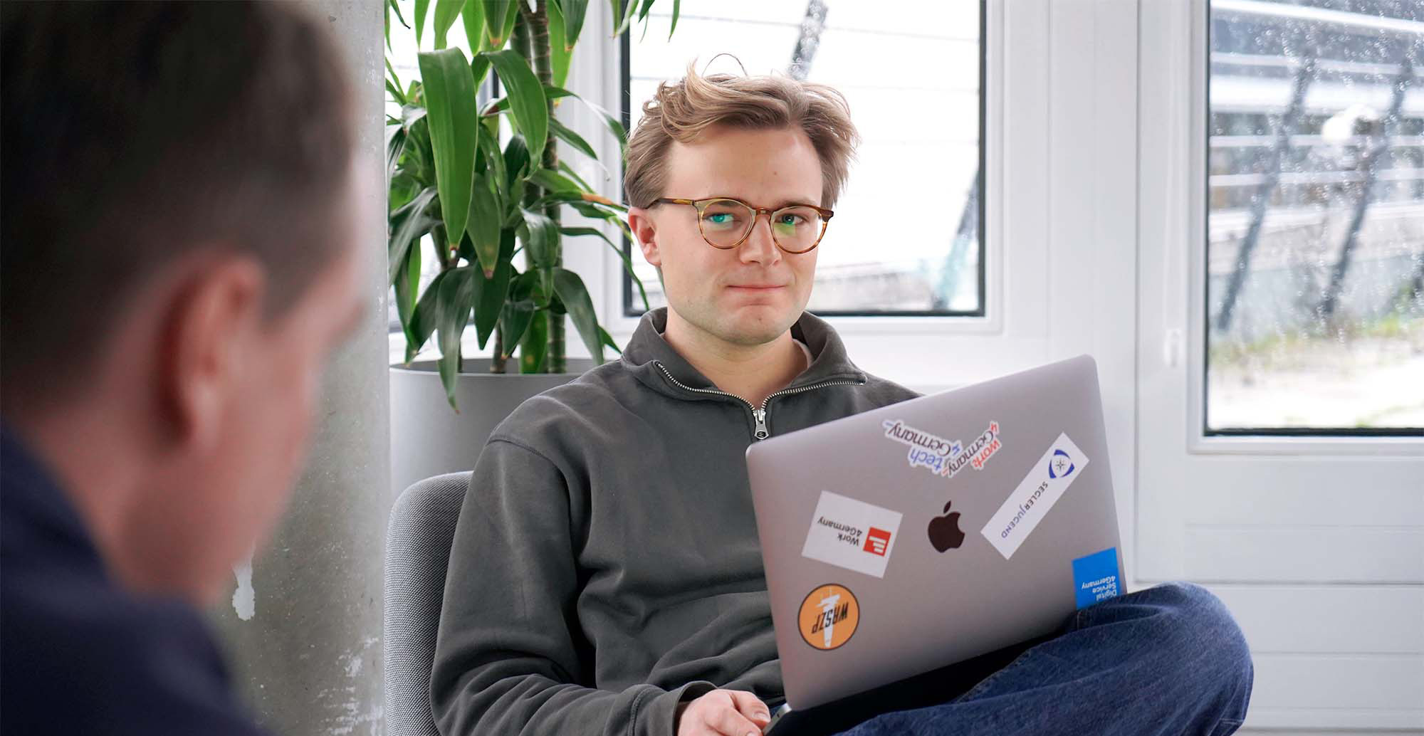 Interview partner Moritz has his laptop on his feet and is sitting in the DigitalService office while talking to a colleague