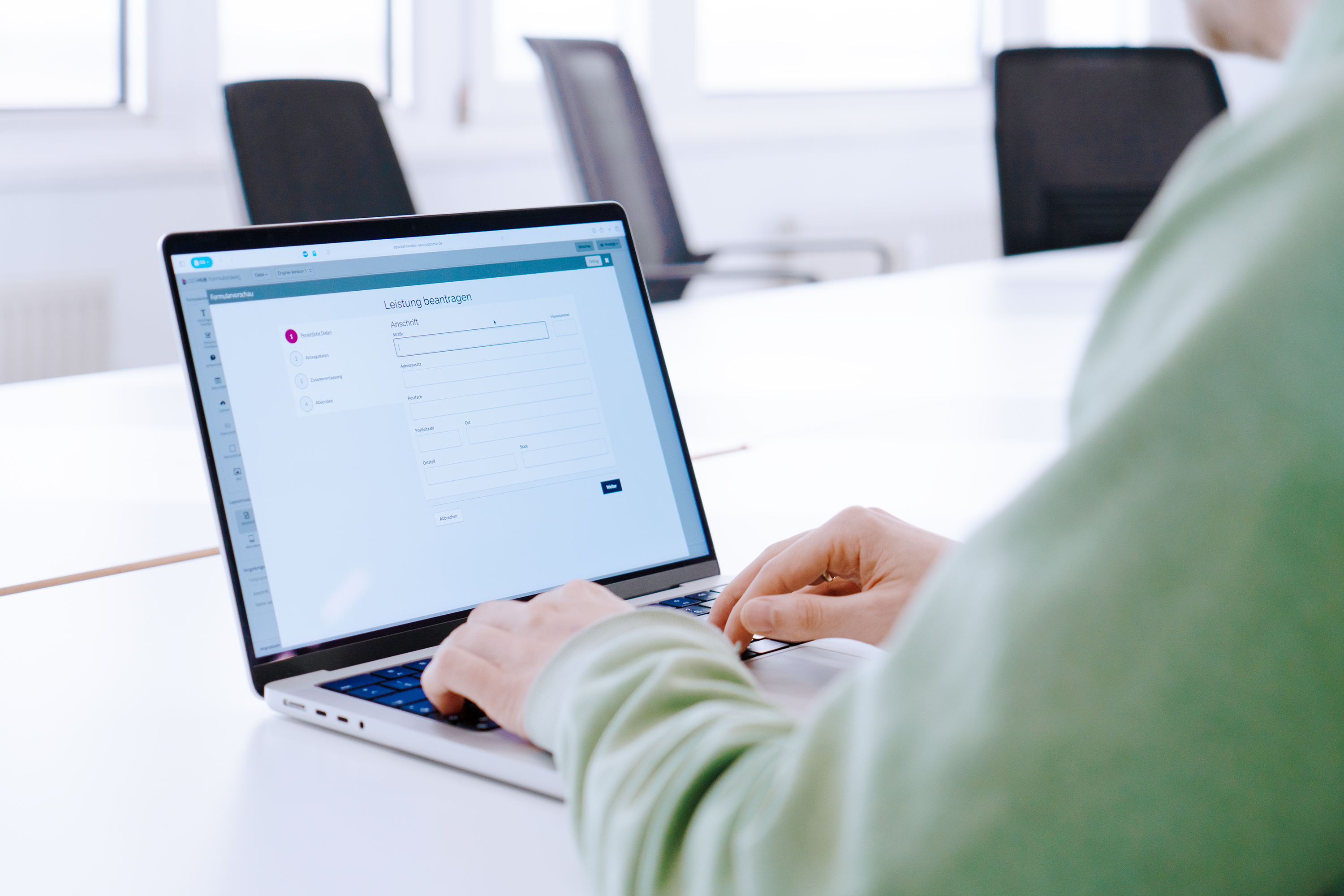 Eine Person sitz an einem Laptop auf dessen Bildschirm ein Formular zu sehen ist mit dem Titel „Leistung beantragen“