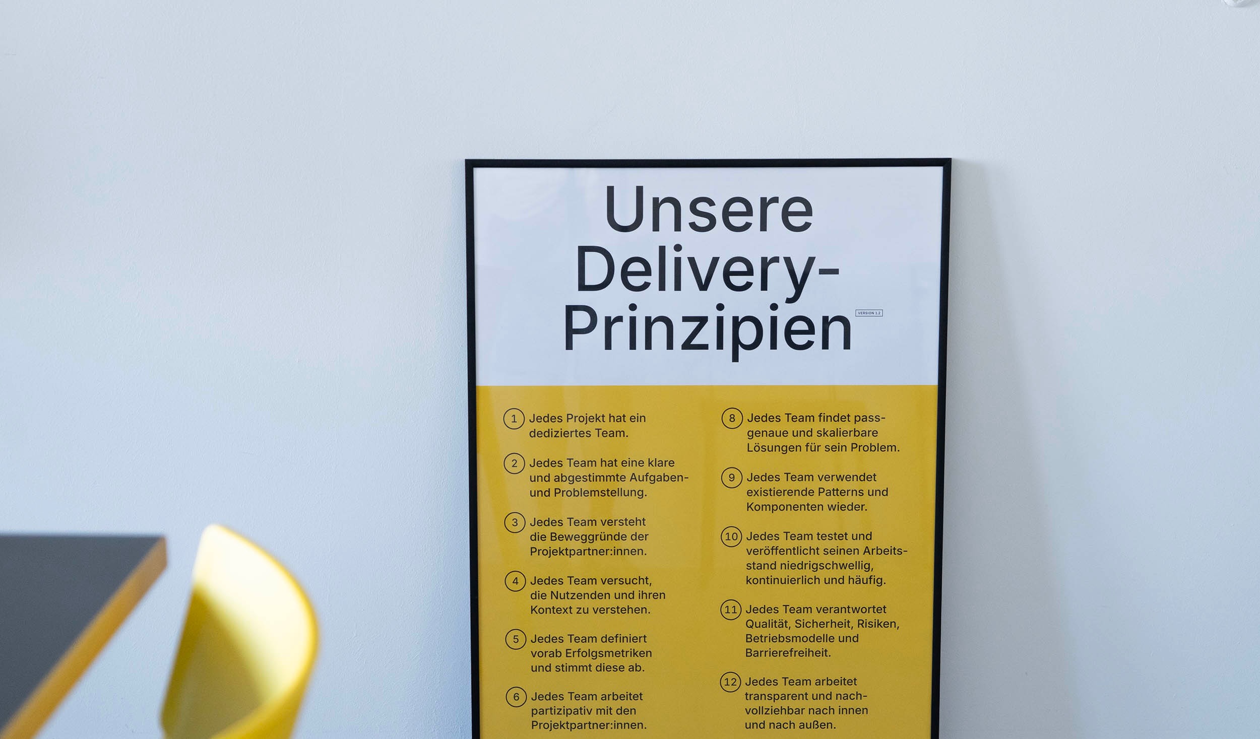 A framed poster of the Delivery Principles leaning against a wall; it lists 12 principles, all but one of which begin with “Every team”; in the lower right corner, the poster refers to the working methods described on the DigitalService website