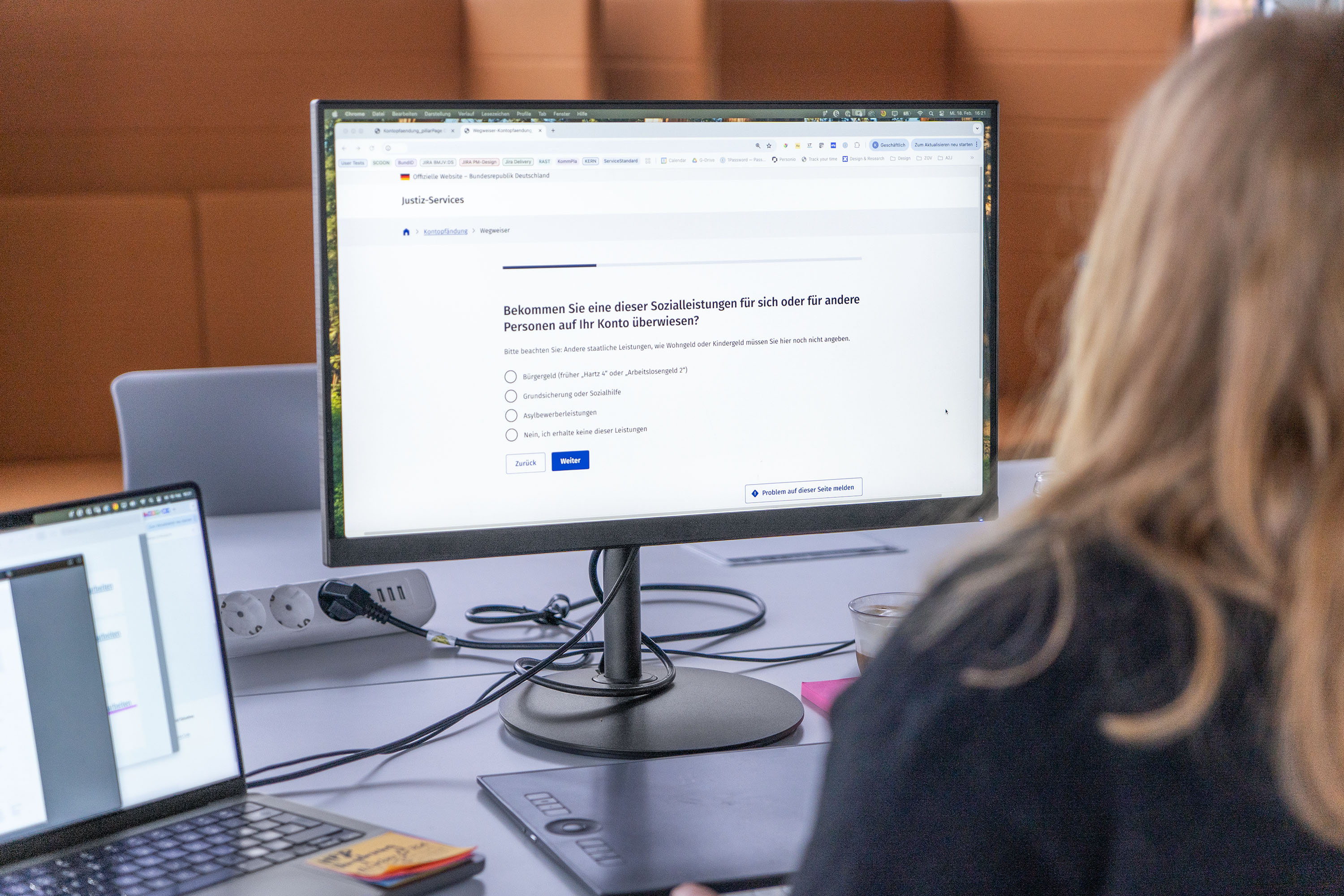 Person vor einem Person sitting in front of a computer monitor displaying a digital legal form and asking a question about receiving social benefits – with 4 different possible answers sitzend, der ein digitales Justizformular zeigt und eine Frage zum Erhalt von Sozialleistungen stellt – mit 4 unterschiedlichen Antwortmöglichkeiten