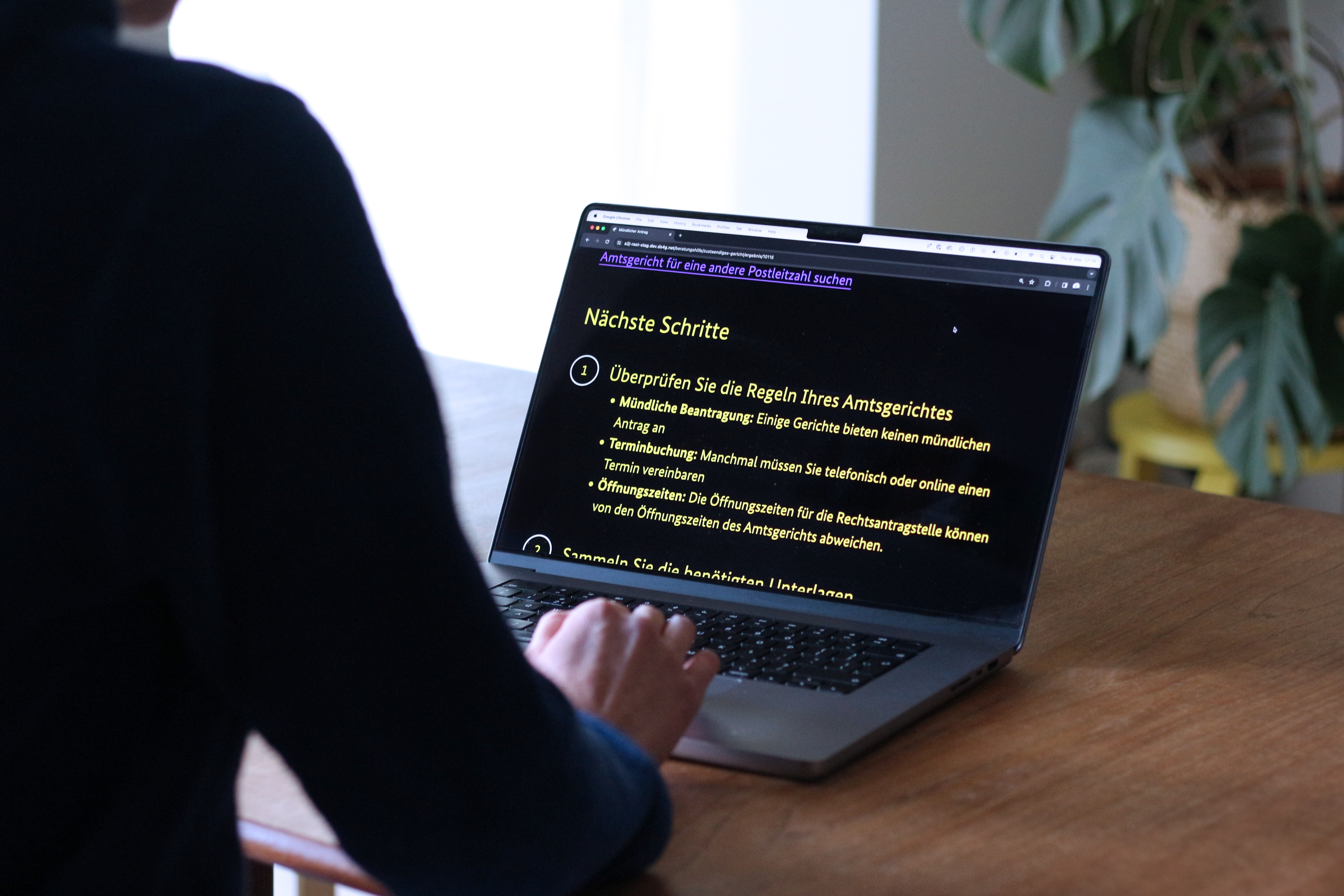 Person at a table with a laptop computer on which a list of local court applications can be seen enlarged in yellow on black