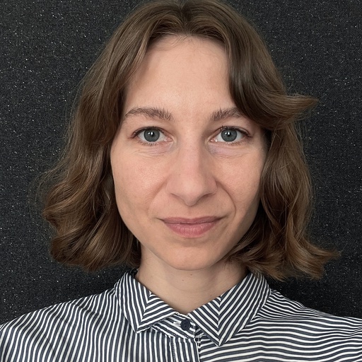 Ann-Kristin Ohlau, UX/UI Designerin beim DigitalService, vor einem dunklen Hintergrund; sie trägt eine schwarz-weiß gestreifte Bluse und hat braune schulterlange Haare