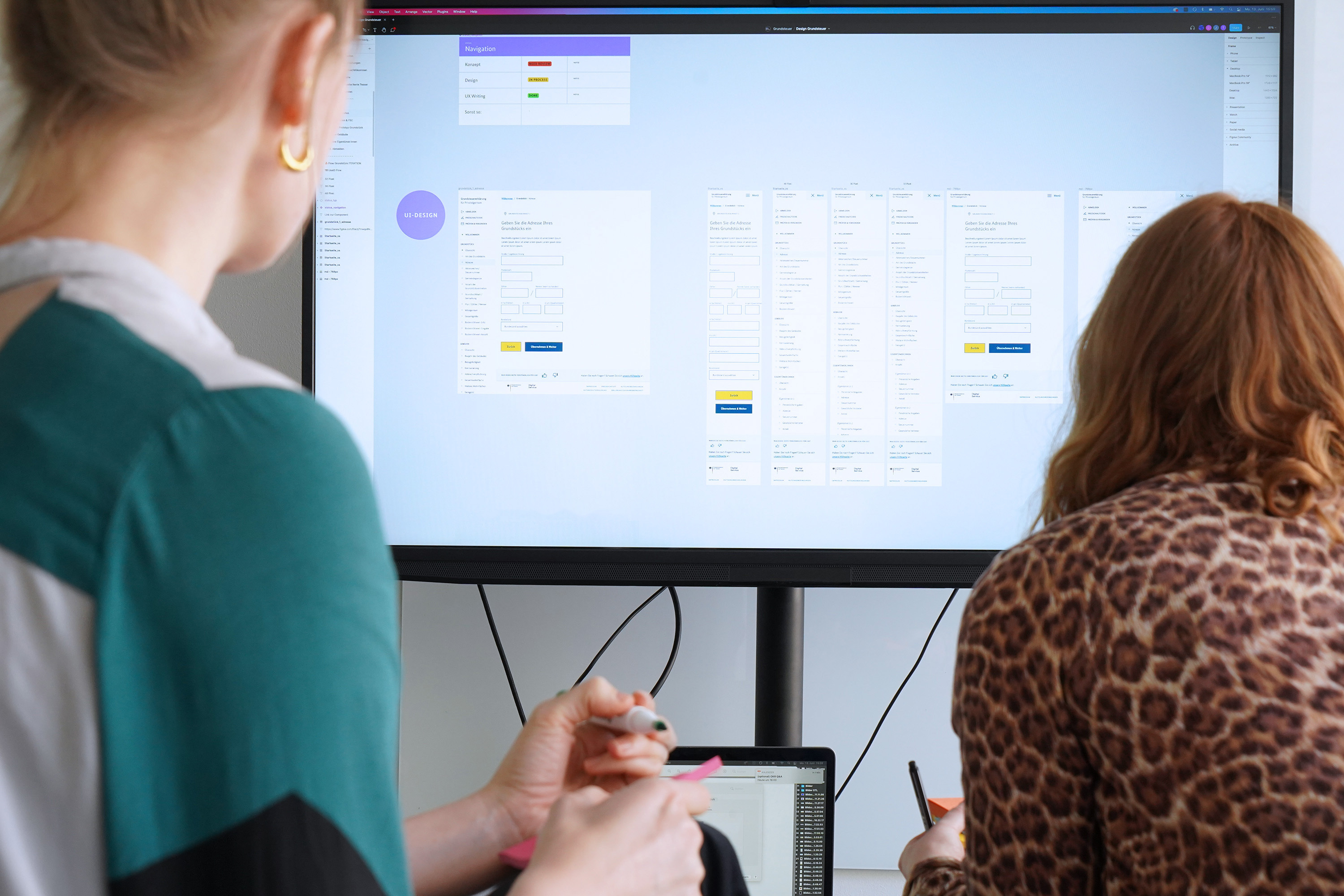 Two people with sticky notes and pens in hand look at a large screen showing different layouts of web pages.