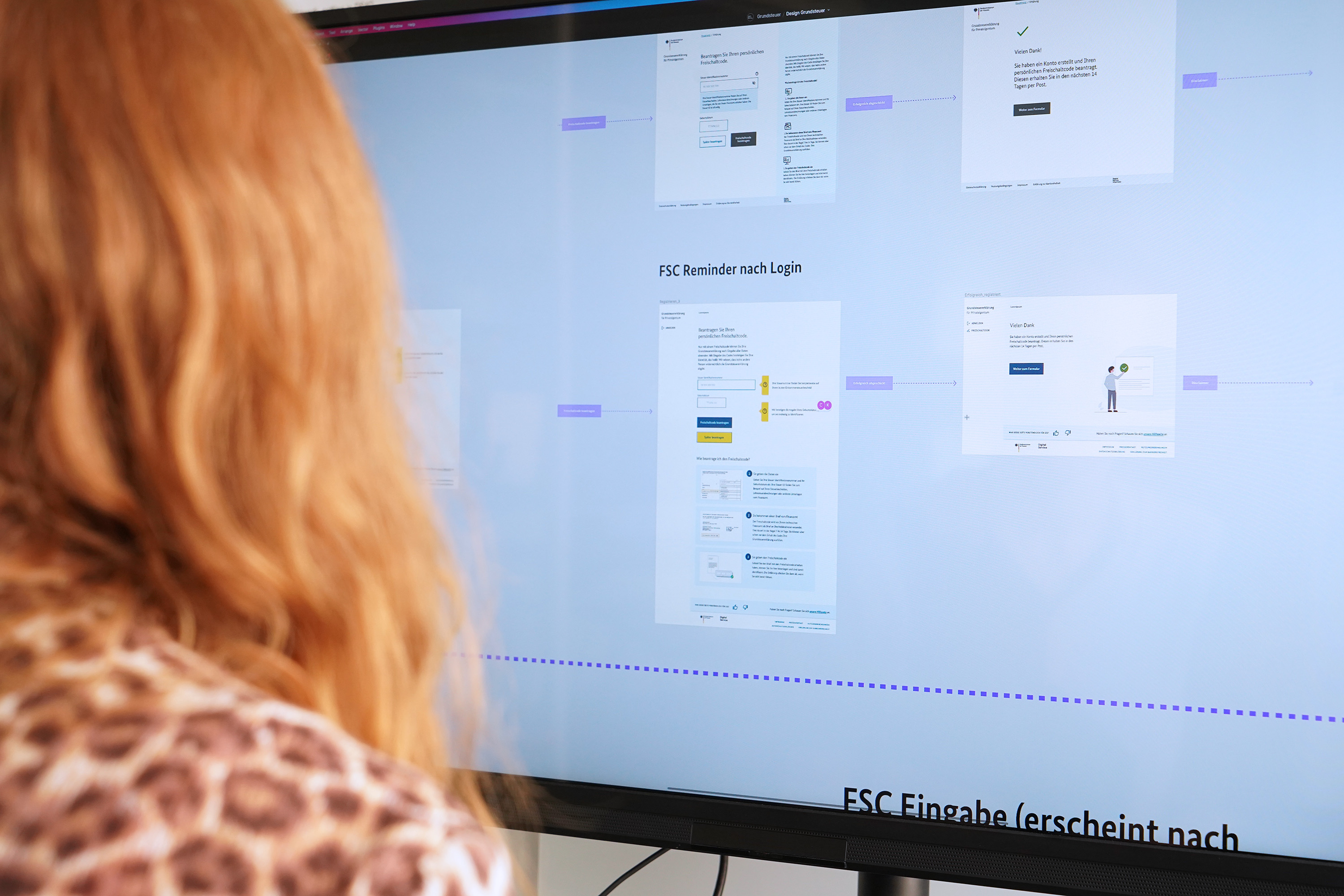 Eine Person mit langen Haaren schaut auf einen großen Bildschirm, der verkleinert eine Sequenz an Seiten eines Online-Verwaltungsservices zeigt