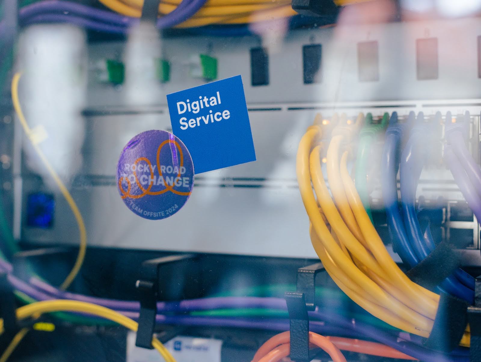Several yellow and blue cables are plugged into a distributor. A sticker with the DigitalService logo and a sticker with the words “Rocky road to change” are stuck to it.