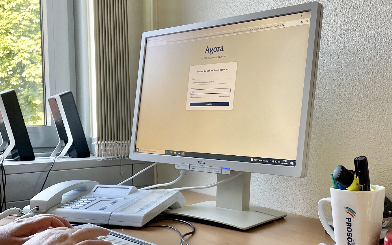 Standrechner mit Browseransicht der Agora-Plattform und Telefon in einem Büro