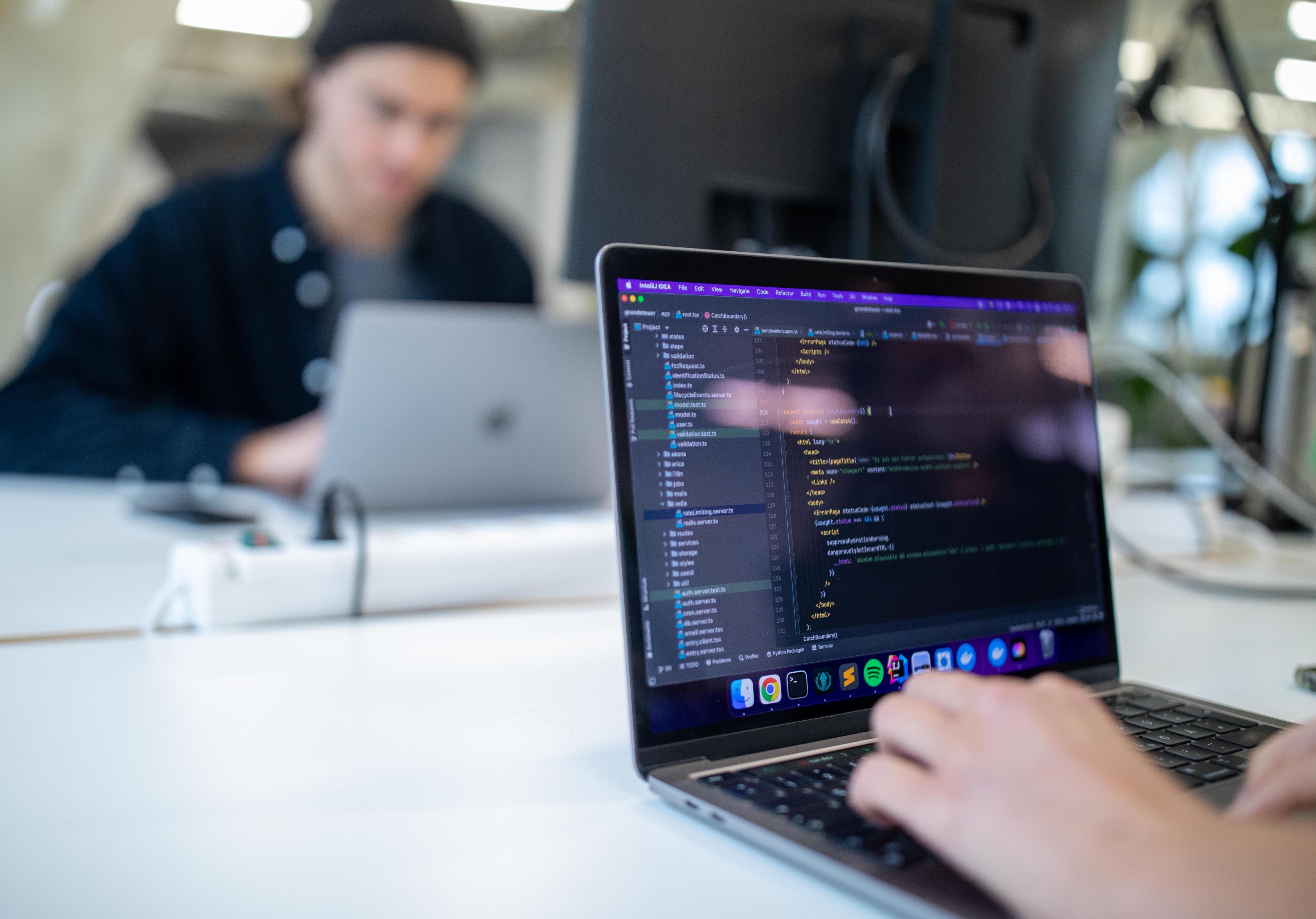 A person writes code on their laptop; the components of the code can be seen in different colors on the open laptop screen