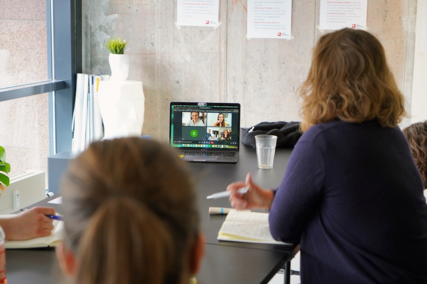 Typical scene from a fellowship: a few participants sit in an office around a long table and talk to other participants via video call.