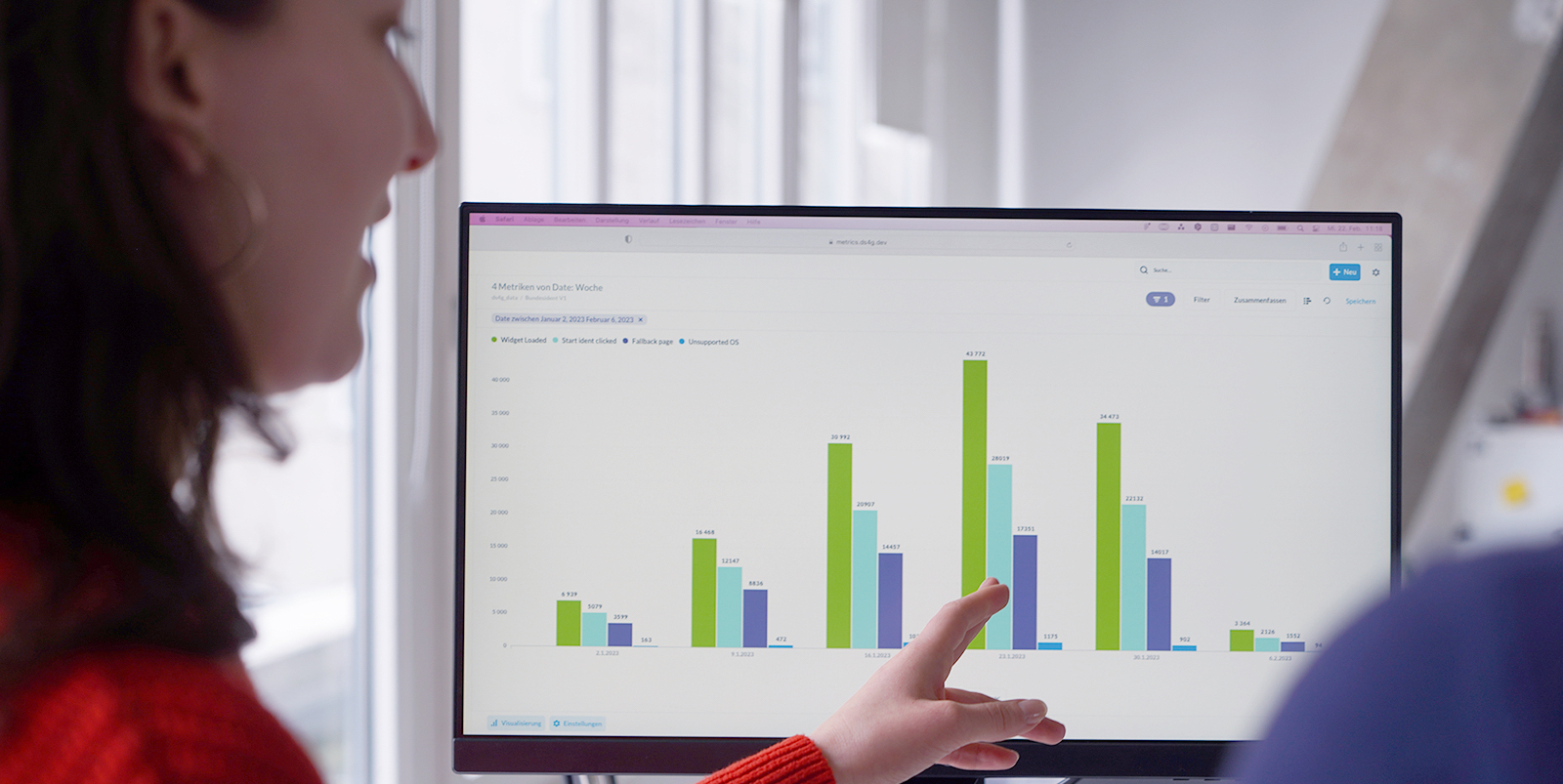 One person points to a block diagram on a screen while talking to another person.