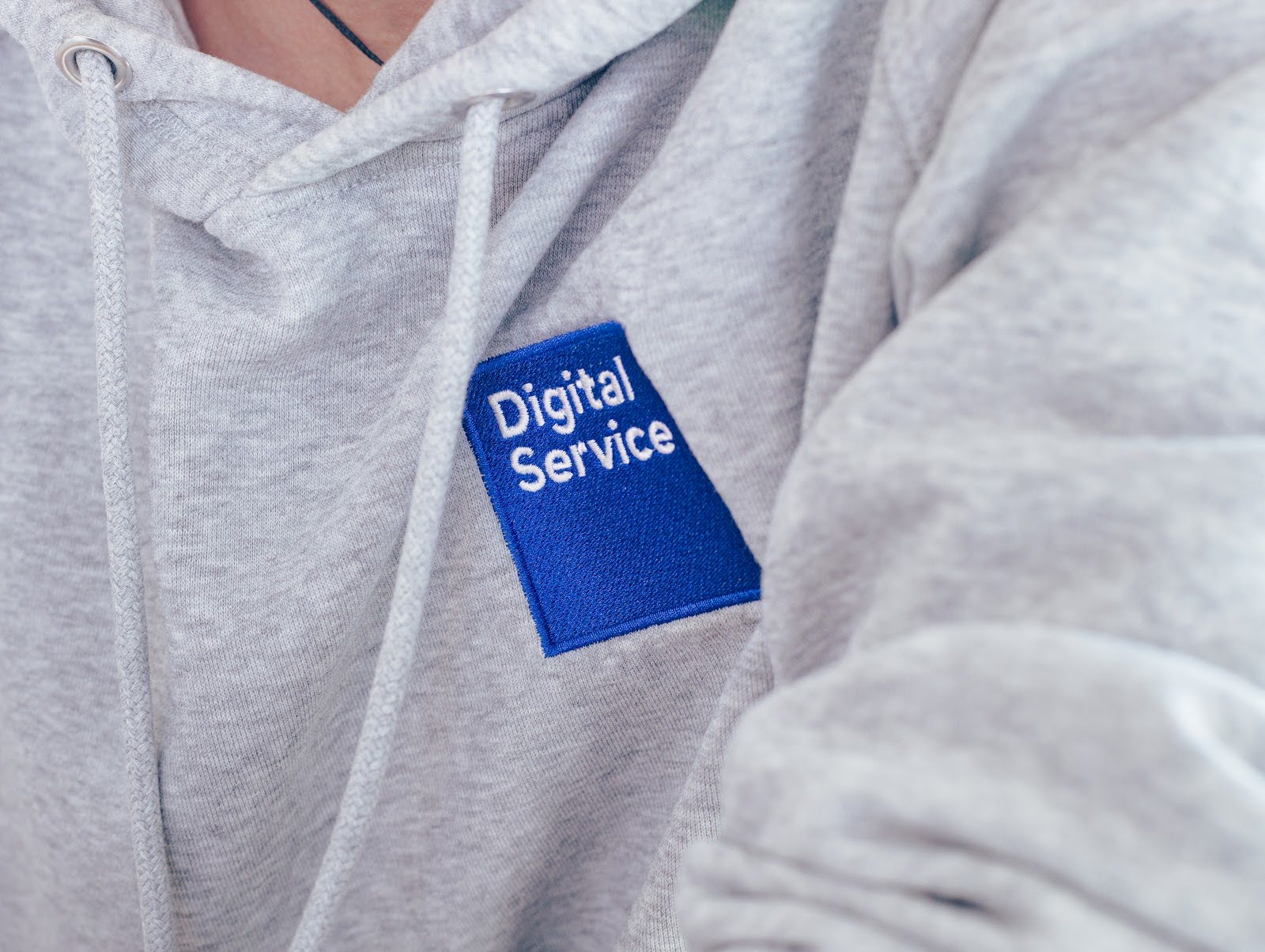 Auf dem Bild ist eine Nahaufnahme eines grauen Pullovers mit dem Logo des DigitalService zu sehen. Das Logo ist ein blaues Viereck mit der weißen Schrift „DigitalService“ in der oberen Hälfte des Logos.