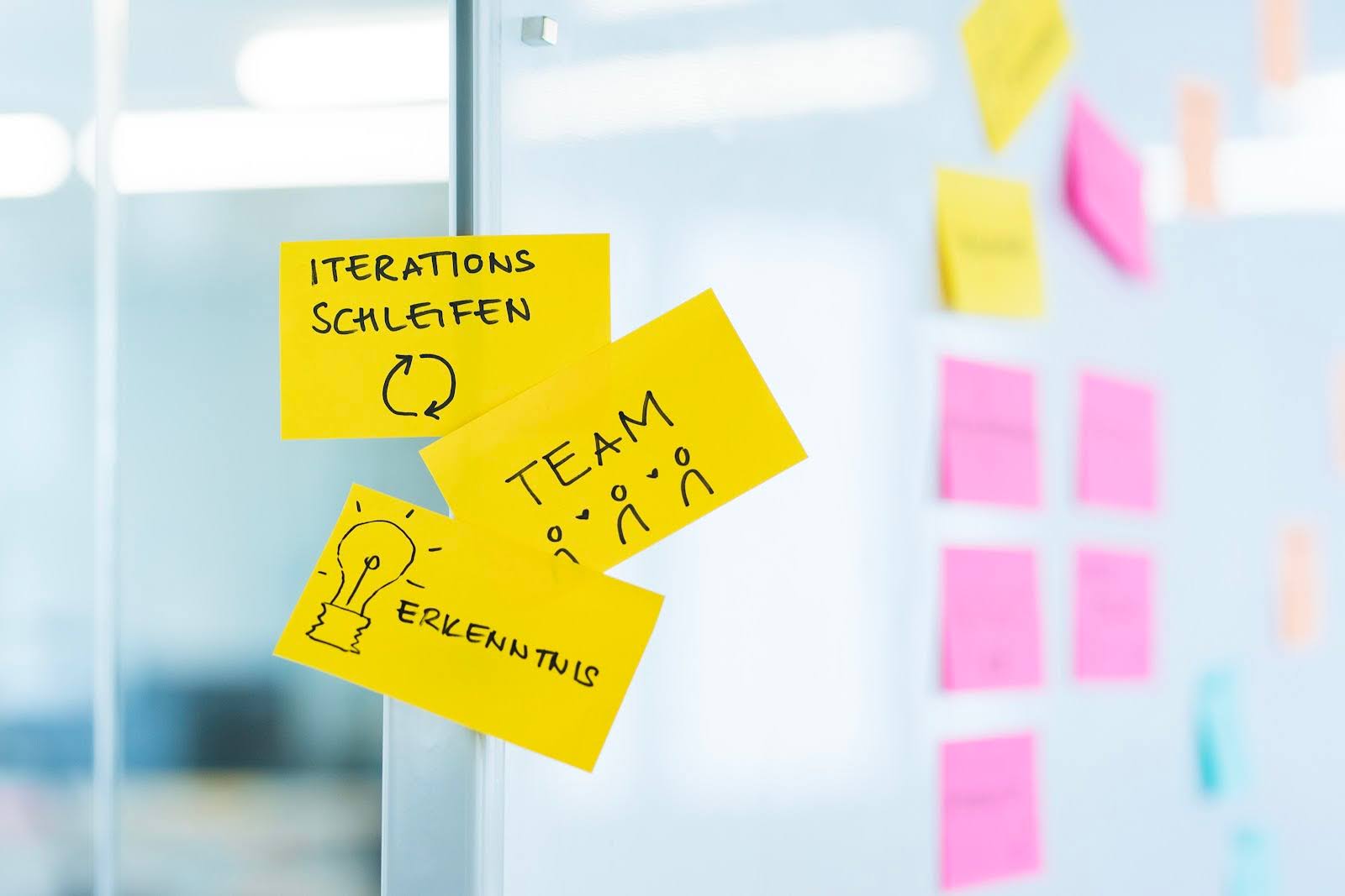Three notes are stuck to a glass wall. The notes say “iteration loops,” “team,” and “insight.”