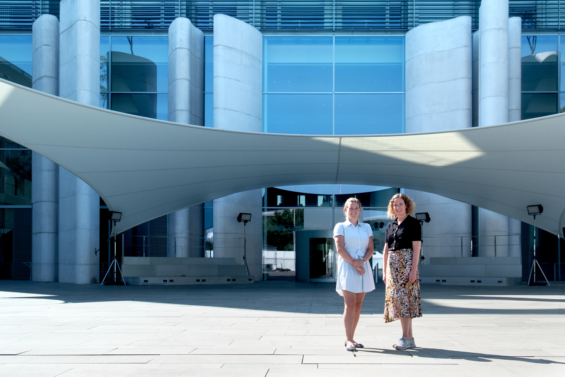 Claudia Straub und Jennifer Rohde stehen gemeinsam in der Sonne vor dem Bundeskanzleramt
