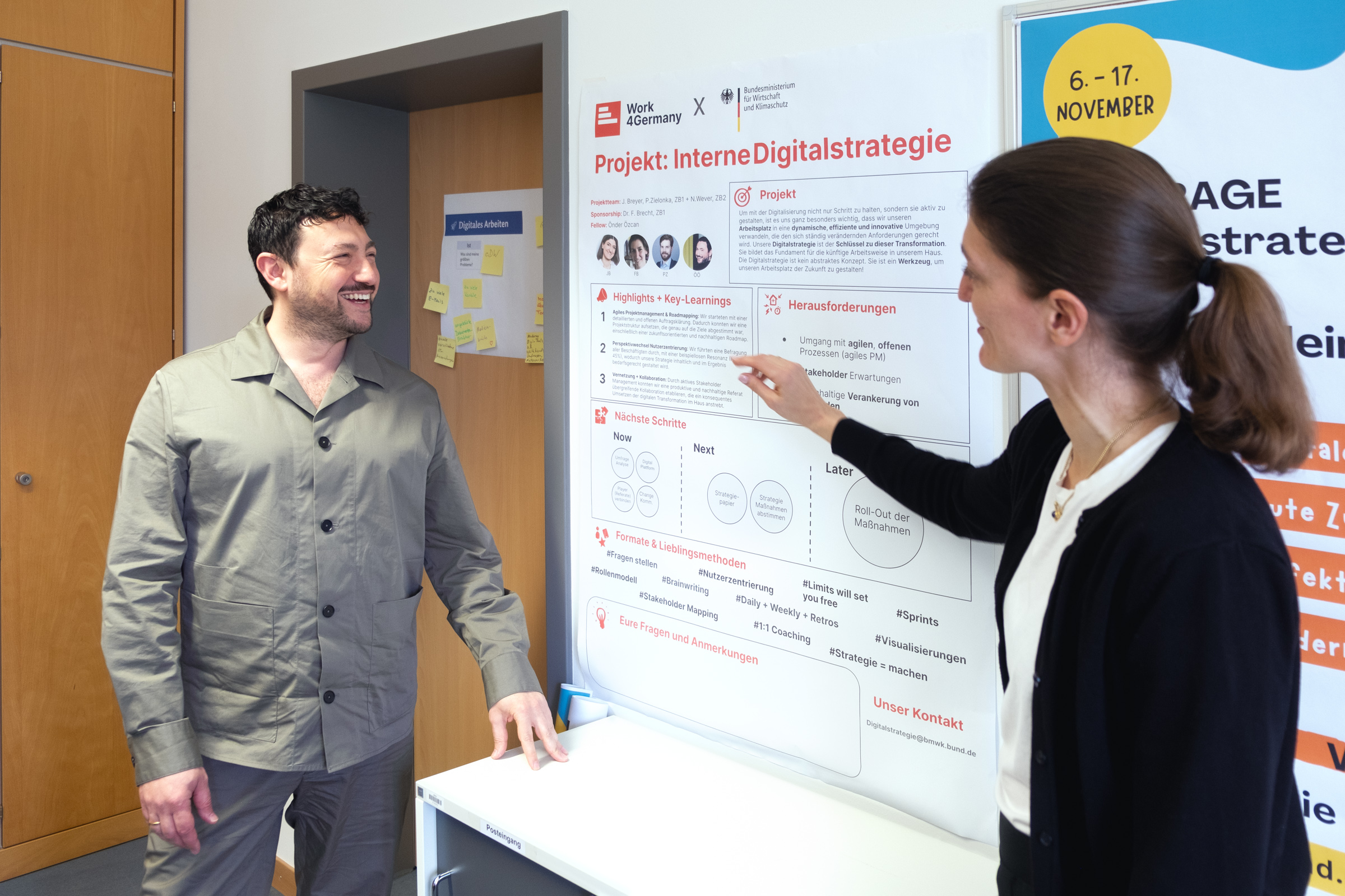 Work4Germany Fellow Önder und seine Projektpartnerin Julia stehen vor einem Plakat mit Informationen zum Projekt „Interne Digitalstrategie“ des Bundesministeriums für Wirtschaft und Klimaschutz