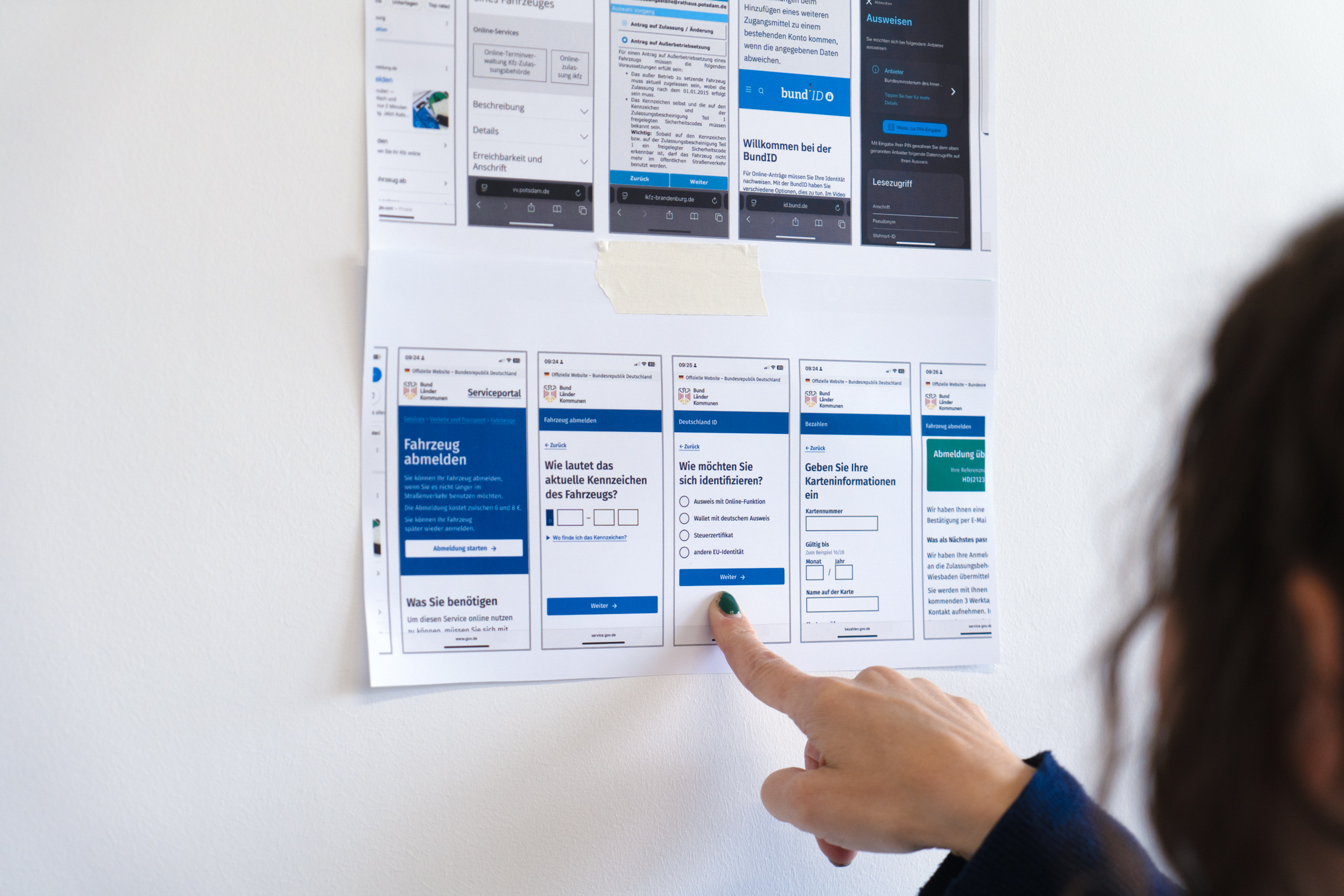 Eine Person zeigt auf einen von zwei Ausdrucken, die zwei Bildschirmreihen zeigen: Die obere Reihe weist sehr unterschiedliche visuelle Designs auf, die untere Reihe hat ein einheitliches Erscheinungsbild für den Dienst „Fahrzeug abmelden“.