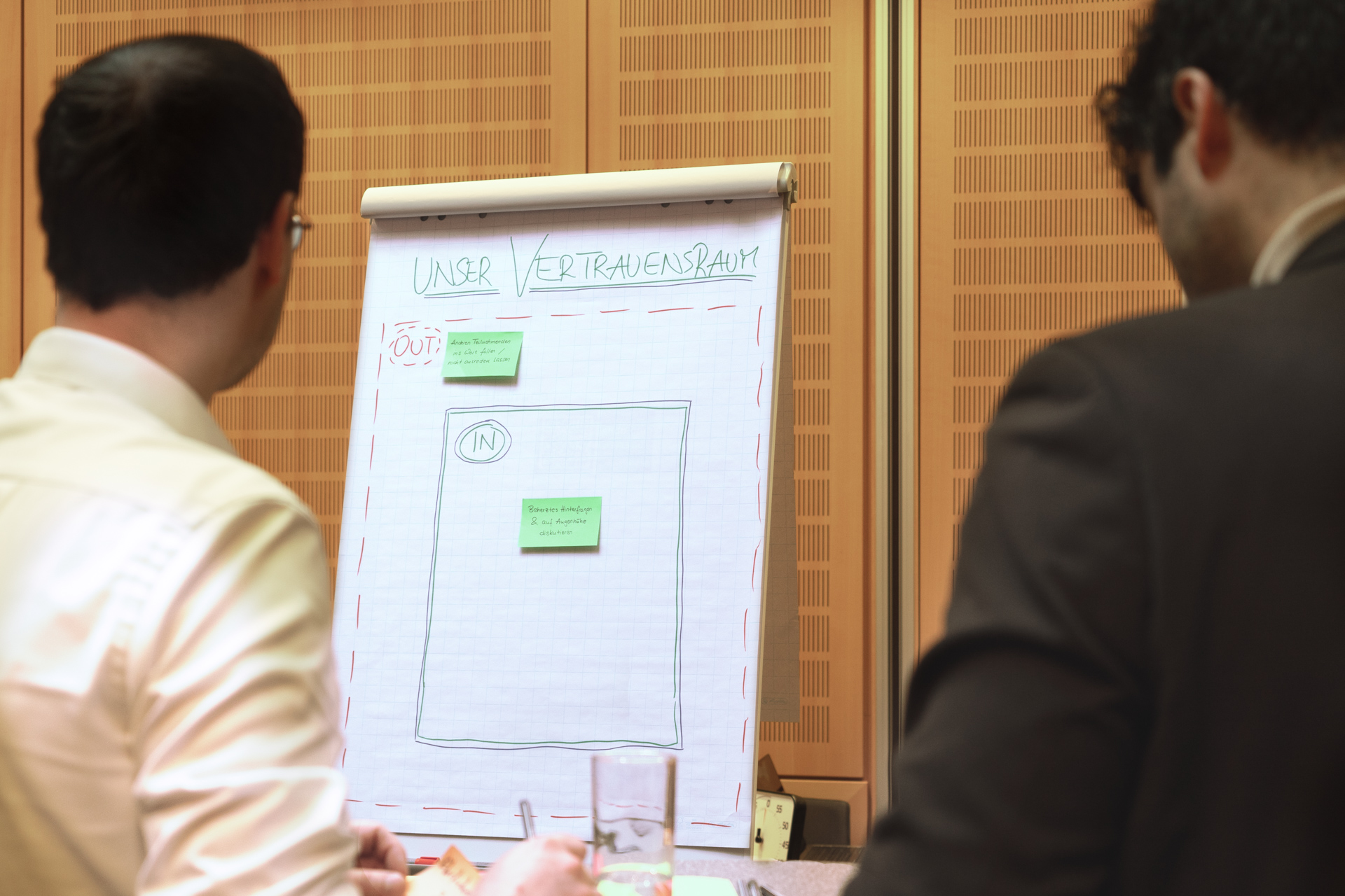 Two people stand in front of a whiteboard on which thoughts on the topic of “trust space” are collected on sticky notes