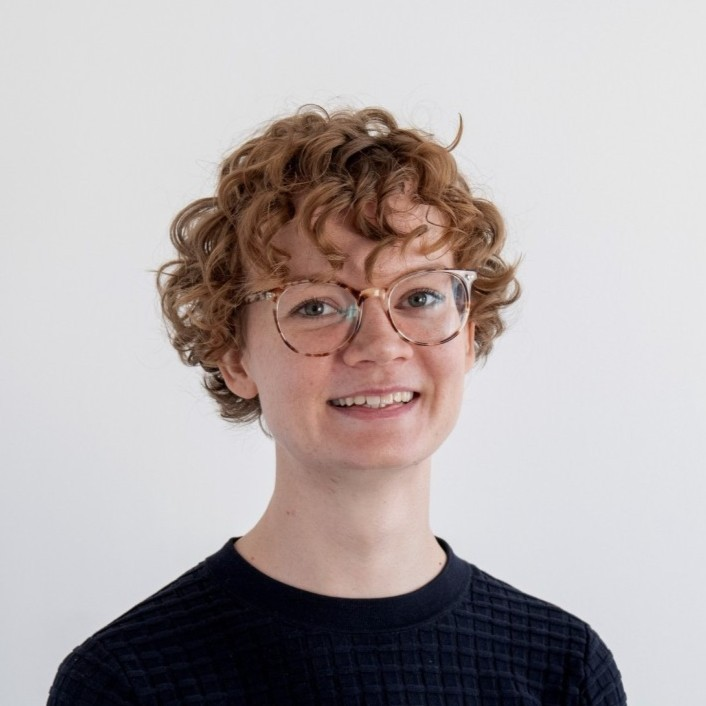 Carina Haumerin, UX Designerin beim DigitalService, steht vor einer weißen Wand. Sie trägt ein schwarzes Oberteil und eine Brille.