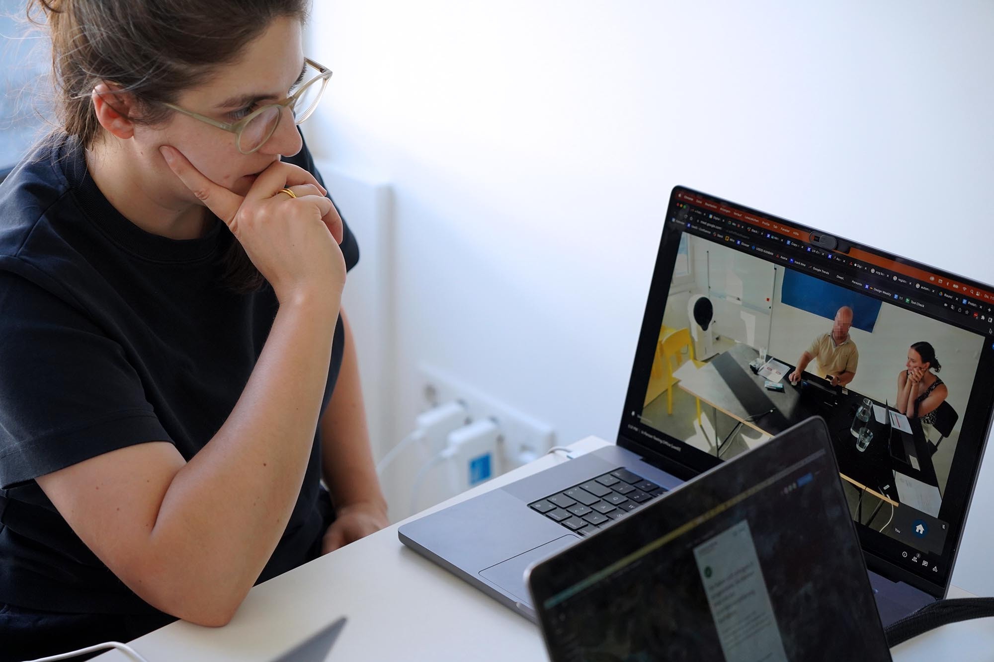 Eine junge Frau im schwarzen T-Shirt schaut konzentriert auf einen Laptop-Computer. Dort sieht man einen Mann und eine Frau, die an einem Tisch sitzen. Der Mann benutzt einen Computer mit einer Maus, die Frau schaut ihm dabei zu.