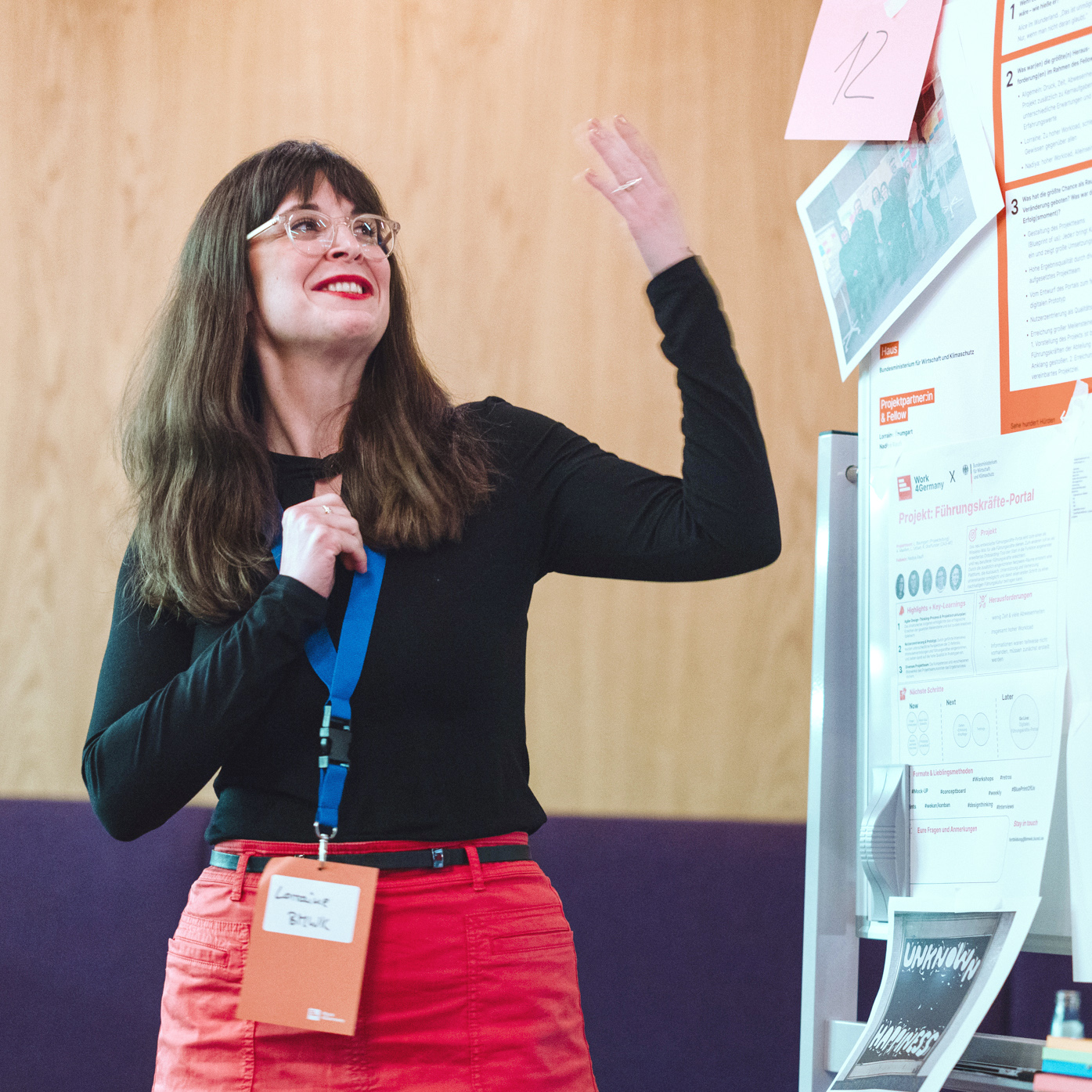 One person stands in front of a wall with lots of notes and posters and explains them gesticulating