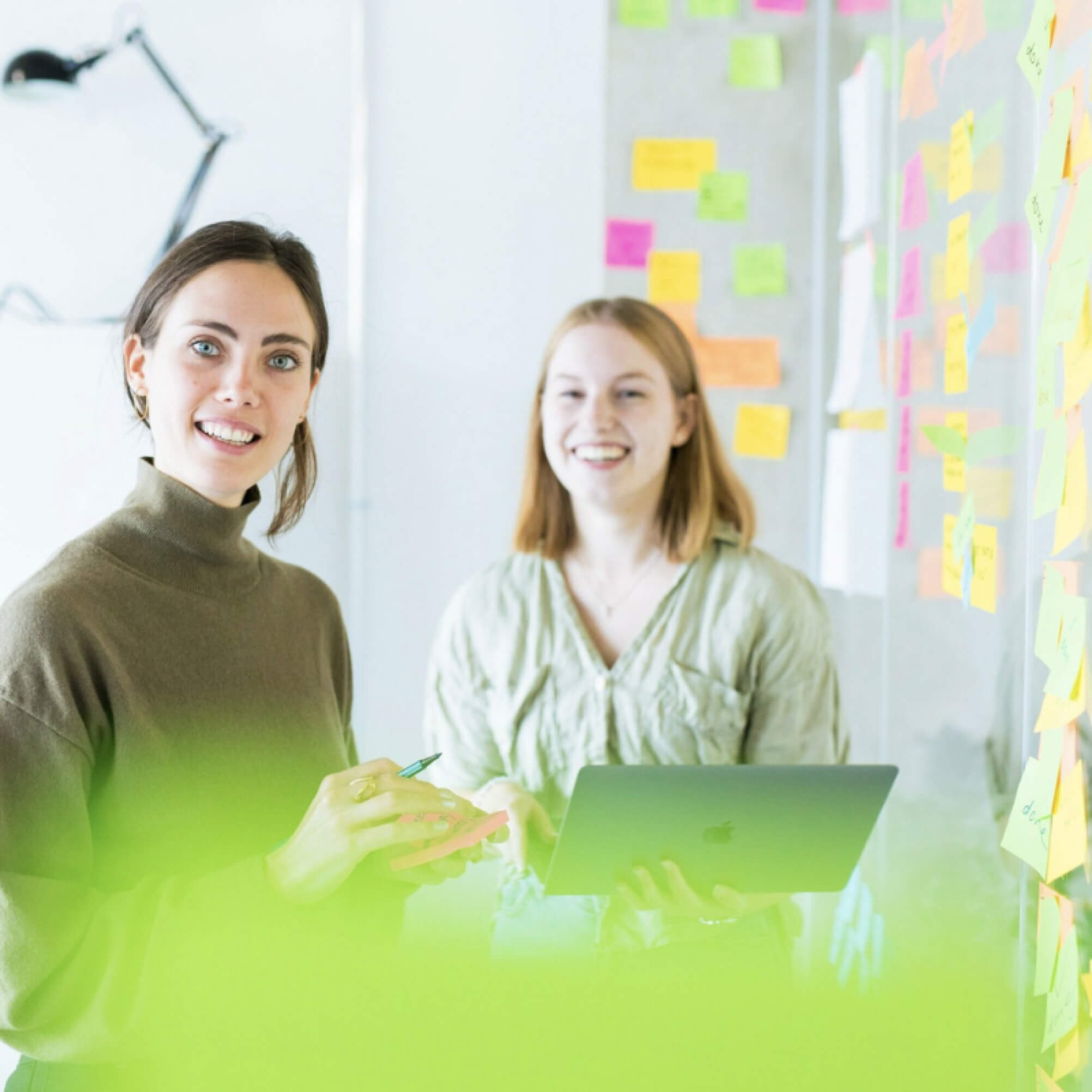 Two DigitalService employees stand in front of a whiteboard with lots of colorful notes stuck to it