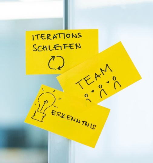 Three notes are stuck to a glass wall. The notes say “iteration loops,” “team,” and “insight.”