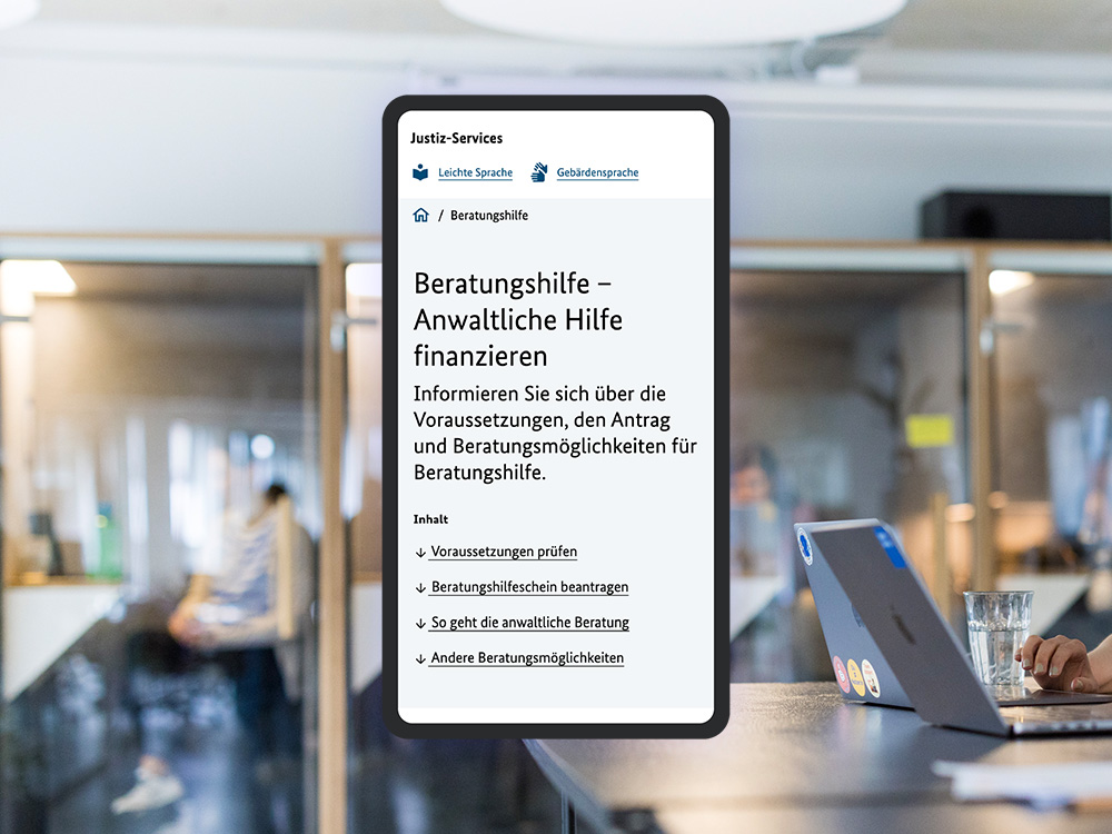 The image shows a cell phone screen displaying a website from service.justiz.de with the title “Beratungshilfe - Anwaltliche Hilfe finanzieren”. In the background is a modern office with glass walls in which a person can be seen out of focus. On the right of the picture you can see a laptop on a table with a glass of water next to it.