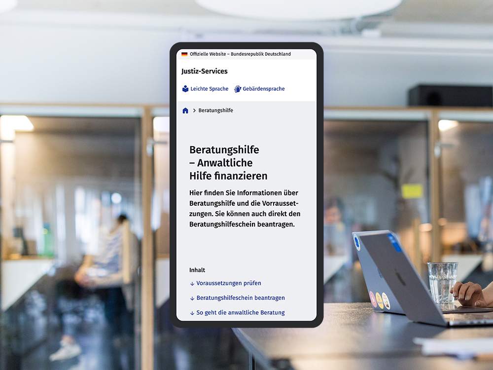 The image shows a cell phone screen displaying a website from service.justiz.de with the title “Beratungshilfe - Anwaltliche Hilfe finanzieren”. In the background is a modern office with glass walls in which a person can be seen out of focus. On the right of the picture you can see a laptop on a table with a glass of water next to it.