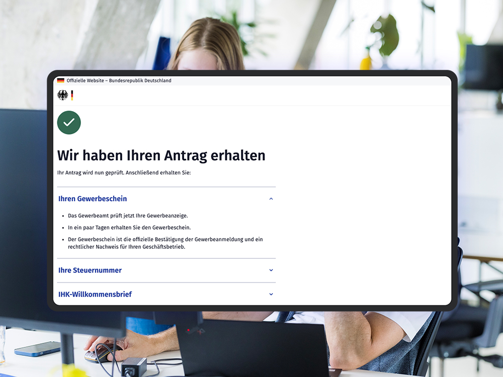 Mockup einer offiziellen deutschen Regierungswebseite mit Bestätigung „Wir haben Ihren Antrag erhalten“. Hinweise zu Gewerbeschein, Steuernummer und IHK-Willkommensbrief sind aufgelistet; als visuelles Stilmittel sieht man im Hintergrund das Büro des DigitalService