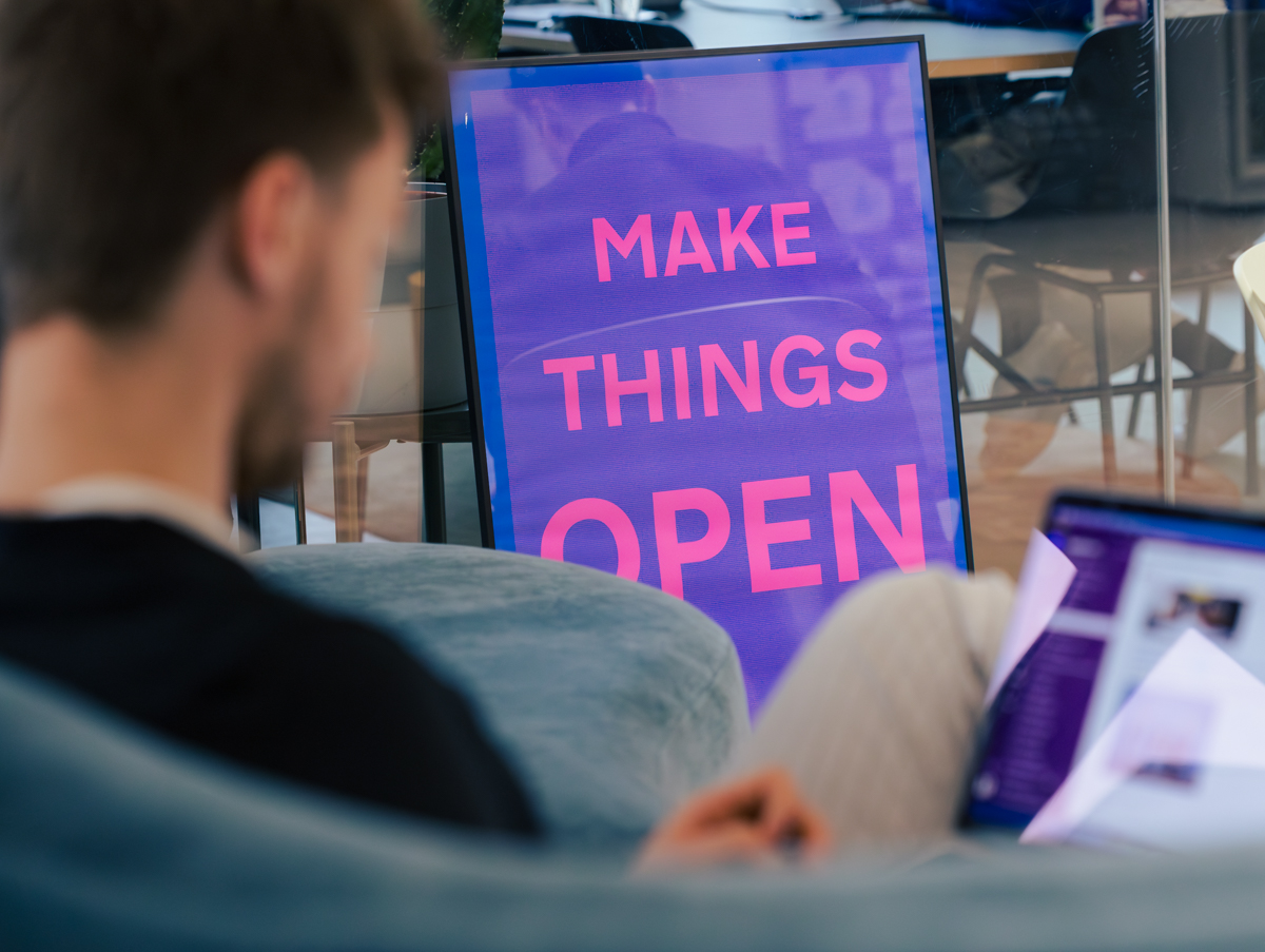 A poster with the slogan “Make Things Open” hangs on a glass wall in the DigitalService office; in the foreground sits a DigitalService employee, who can be seen as a silhouette.